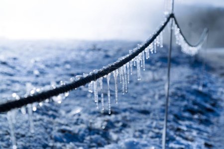 Foto de Un primer plano de carámbanos colgando de un alambre congelado en el fondo de la tierra congelada - Imagen libre de derechos