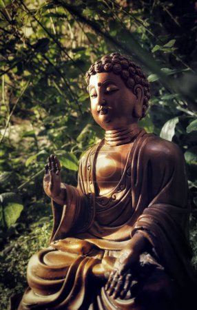 Photo for A vertical shot of brown buddha statue in meditation in the forest with green plants in the background - Royalty Free Image
