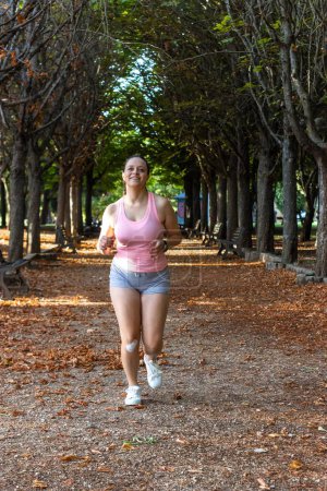 Téléchargez les photos : Plan vertical d'une jolie femme sportive qui court et sourit dans un parc d'automne - en image libre de droit