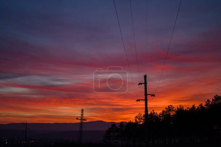 Foto de Una vista espectacular del cielo al atardecer, líneas eléctricas y siluetas de estaciones contra nubes púrpuras - Imagen libre de derechos