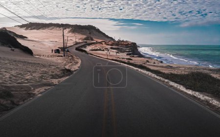 Foto de Un camino de carretera en un paisaje árido cerca del mar bajo el cielo azul nublado - Imagen libre de derechos