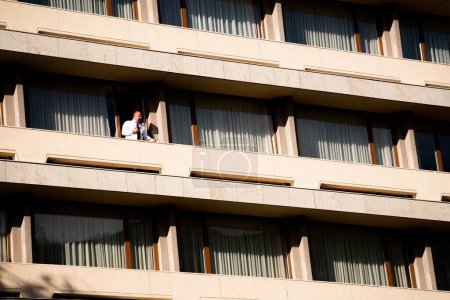 Foto de Un hombre de mediana edad fumando en el balcón de un edificio de apartamentos de estilo comunista - Imagen libre de derechos