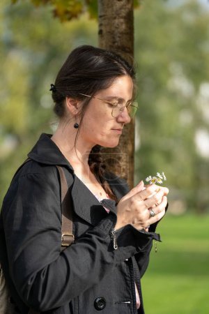 Photo for A vertical shot of a white female wearing specs and looking at the small flowers in her hands - Royalty Free Image