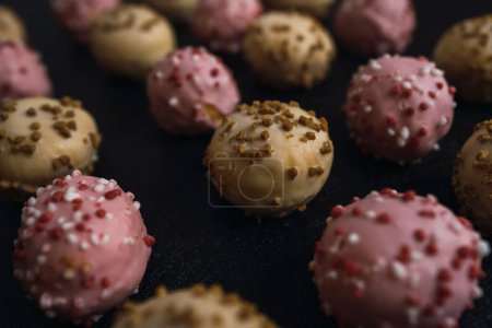 Foto de Un primer plano de deliciosas bolas de pastel rosado y marrón con glaseado colorido aislado sobre un fondo oscuro - Imagen libre de derechos