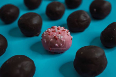 Photo for A closeup of delicious chocolate cake balls with a pink one standing out in the middle on a blue background - Royalty Free Image