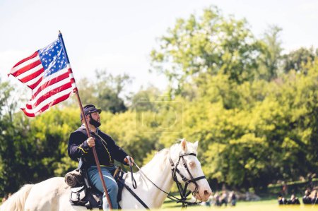Foto de Un soldado montando un caballo y levanta la bandera de Estados Unidos durante el desempeño militar en la recreación de la guerra civil en la ciudad de Jackson, Michigan, EE.UU. - Imagen libre de derechos