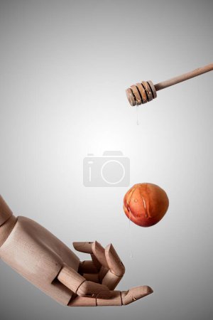 Foto de Un disparo vertical de un palo de miel que gotea miel sobre un melocotón sobre una mano modelo de madera - Imagen libre de derechos