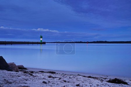 Foto de Un faro a una distancia vista desde la playa de arena Travemuende durante la tranquila puesta de sol azul - Imagen libre de derechos