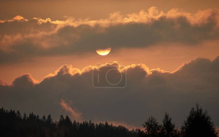 Téléchargez les photos : Le soleil doré brille sur la forêt ombragée dans le ciel nuageux pendant le coucher du soleil - en image libre de droit
