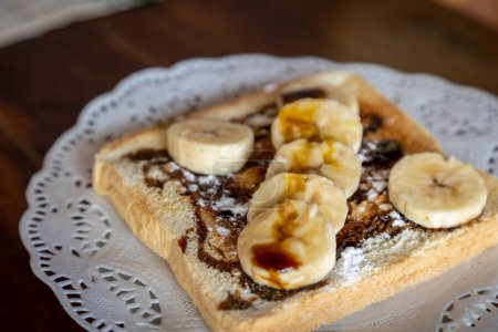 Téléchargez les photos : Gros plan horizontal d'un pain grillé avec des morceaux de chocolat et de banane sur une assiette blanche sur une table en bois - en image libre de droit