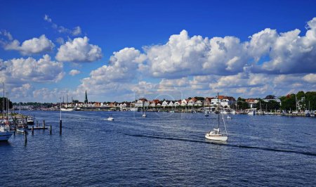 Téléchargez les photos : Un bateau naviguant sur la rivière Trave entouré de bâtiments traditionnels lors d'une journée d'été en Allemagne - en image libre de droit
