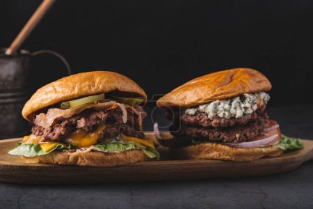 Foto de Un primer plano de hamburguesas dobles sobre un tablero de madera sobre un fondo negro - Imagen libre de derechos