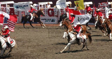 Téléchargez les photos : Les cow-girls sur les chevaux tenant les drapeaux des participants au rodéo au Stampede de Calgary, Canada - en image libre de droit