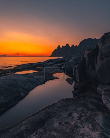 Foto de Un tiro vertical de mar desde una costa rocosa y montaña en el fondo durante la puesta del sol - Imagen libre de derechos