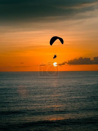 Foto de Una silueta de una persona parapente sobre una costa al atardecer - Imagen libre de derechos