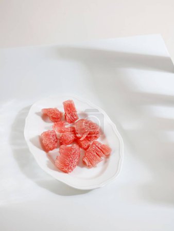 Foto de Una toma vertical de un plato de piezas de pomelo rojo sobre una mesa blanca - Imagen libre de derechos