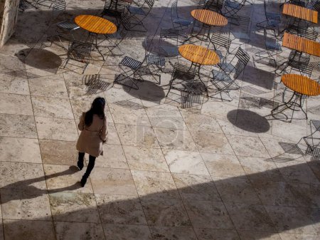 Foto de Una mujer caminando por un comedor vacío al aire libre con suelos de mármol y mesas de madera - Imagen libre de derechos