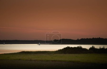Foto de Un lago tranquilo con un barco nadando en él rodeado por el bosque oscuro bajo el cielo atardecer - Imagen libre de derechos