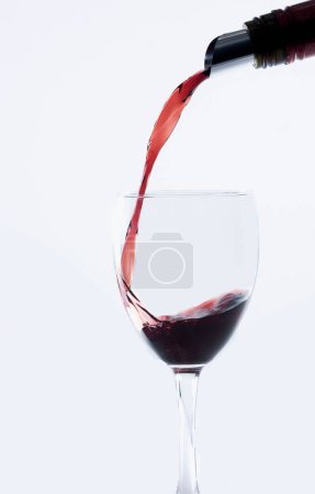 Téléchargez les photos : Une bouteille de vin rouge coulant sur un verre de vin isolé sur fond blanc, plan vertical - en image libre de droit
