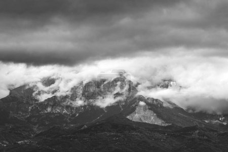 Téléchargez les photos : Échelle de gris d'un sommet de montagne couvert de brouillard avec un ciel nuageux dramatique en arrière-plan - en image libre de droit