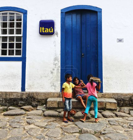 Foto de Varios niños jugando y divirtiéndose frente a una puerta azul de un edificio blanco en el casco antiguo de Paraty en Brasil - Imagen libre de derechos