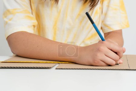 Foto de Una niña dibujando con un lápiz sobre cartón con la ayuda de la medida sobre un fondo blanco - Imagen libre de derechos