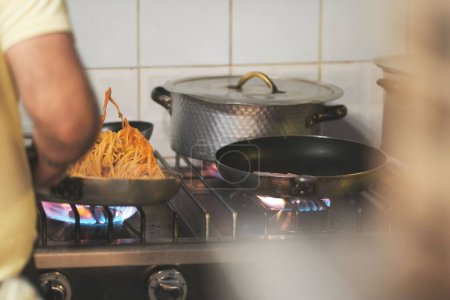 Foto de Un buen tiro de un macho preparando espaguetis en un frypan, con otras ollas en la cocina con llamas en - Imagen libre de derechos