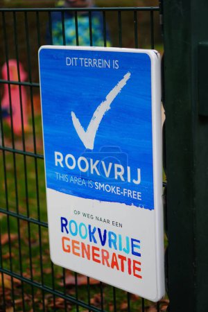 Téléchargez les photos : Un plan vertical de signe en langue néerlandaise indiquant que la zone est sans fumée par une aire de jeux - en image libre de droit