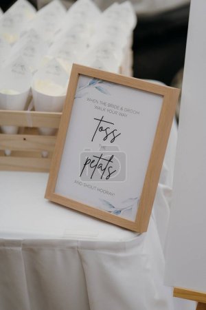 Photo for A vertical shot of a wooden frame informing to toss the petals when the bride and groom walk your way - Royalty Free Image