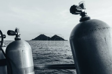 Téléchargez les photos : Une échelle de gris des bouteilles de réservoir pour la plongée sous-marine avec une mer et une île en arrière-plan - en image libre de droit