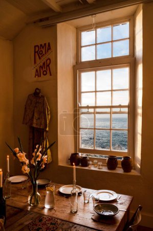 Photo for A vertical shot of a living room with a wooden table with a window overlooking the sea - Royalty Free Image