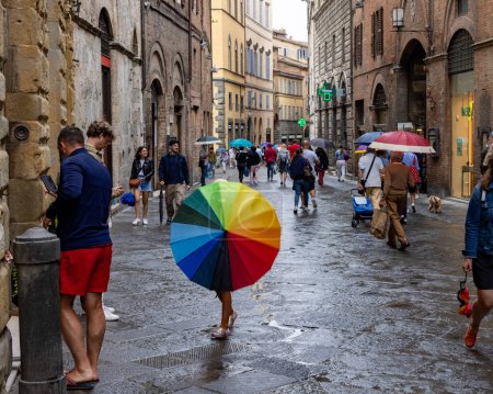 Photo for A girl with a rainbow umbrella walking on a cobbled street in Sienna on a rainy day - Royalty Free Image