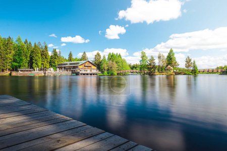 Téléchargez les photos : La surface lisse du lac avec des arbres verts et un bâtiment en bois sur la rive. - en image libre de droit