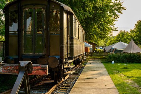Téléchargez les photos : Un wagon de train vintage sur chemin de fer métallique dans le jardin avec de l'herbe et des arbres par une journée ensoleillée - en image libre de droit