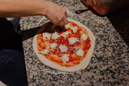 Téléchargez les photos : Un gros plan de mains féminines mettant du fromage sur la pizza dans la cuisine, processus de cuisson de la pizza - en image libre de droit