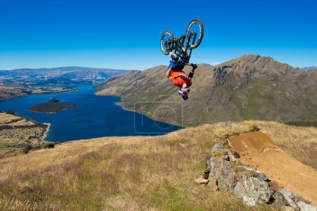 Photo for A man doing a backflip on a Mountain Bike with the beautiful lake and the hills in the background - Royalty Free Image