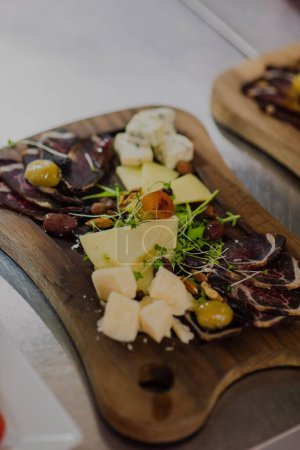 Téléchargez les photos : Un gros plan de fromage et de viande décoré de vert sur une planche de bois sur une table blanche, fond flou - en image libre de droit