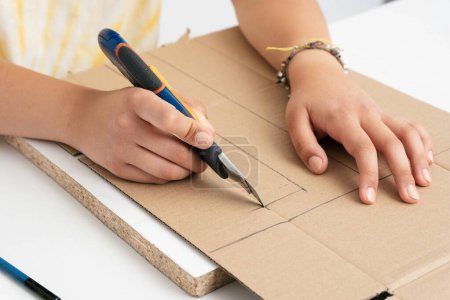 Foto de Un primer plano de una niña cortando cartón con un cortador sobre una gruesa superficie blanca sobre un fondo blanco - Imagen libre de derechos
