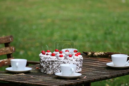 Foto de Una mesa de picnic de madera con un pastel y tazas de té en un parque verde - Imagen libre de derechos