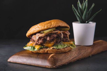 Téléchargez les photos : Gros plan d'un hamburger sur une planche de bois avec une plante en arrière-plan - en image libre de droit