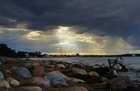 Foto de Una imagen de una costa con piedras y edificios en el fondo con un hermoso cielo - Imagen libre de derechos