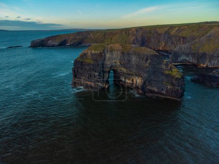Téléchargez les photos : Un coup de drone de falaises rocheuses naturellement formatées dans la mer sous un ciel nuageux bleu au coucher du soleil - en image libre de droit