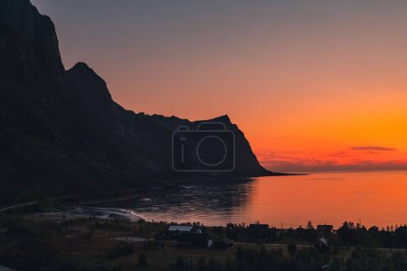 Téléchargez les photos : Un beau plan de petites maisons au bord de la mer avec montagne rocheuse au coucher du soleil dans le nord de la Norvège - en image libre de droit