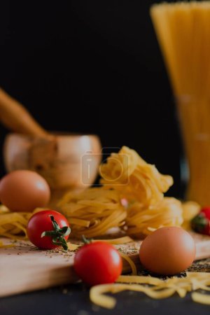 Téléchargez les photos : Une planche de bois avec des pâtes, des tomates cerises, deux œufs et un bol à broyer, saupoudré d'épices - en image libre de droit