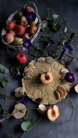 Photo for A vertical shot of a freshly baked pie next to a basket of apples and dry flowers on the table - Royalty Free Image