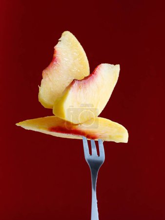 Photo for A closeup of peach slices on a fork in a maroon background - Royalty Free Image