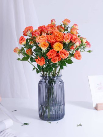 Téléchargez les photos : Plan vertical d'un beau bouquet de roses dans un vase en verre bleu sur une table blanche - en image libre de droit