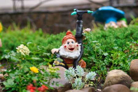 Photo for A close-up shot of a red-hatted garden dwarf placed next to a water sprinkler - Royalty Free Image