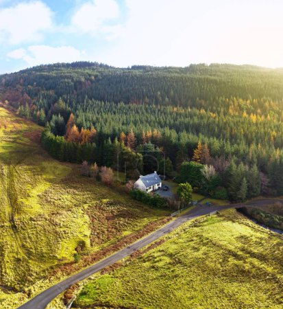 Téléchargez les photos : Un drone tiré d'une maison rurale blanche dans un champ en face d'une forêt à côté d'une route asphaltée - en image libre de droit