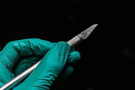 Téléchargez les photos : Un gros plan de la main d'un chirurgien dans un gant en plastique vert tenant un scalpel - en image libre de droit